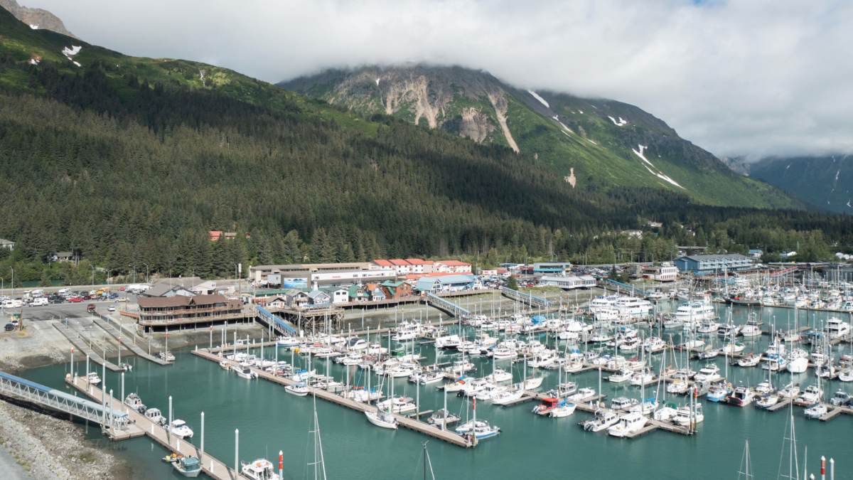 Aerial view of Seward Harbor and Breeze Inn Hotel in Seward, Alaska, surrounded by mountains and filled with fishing boats and tour vessels.
