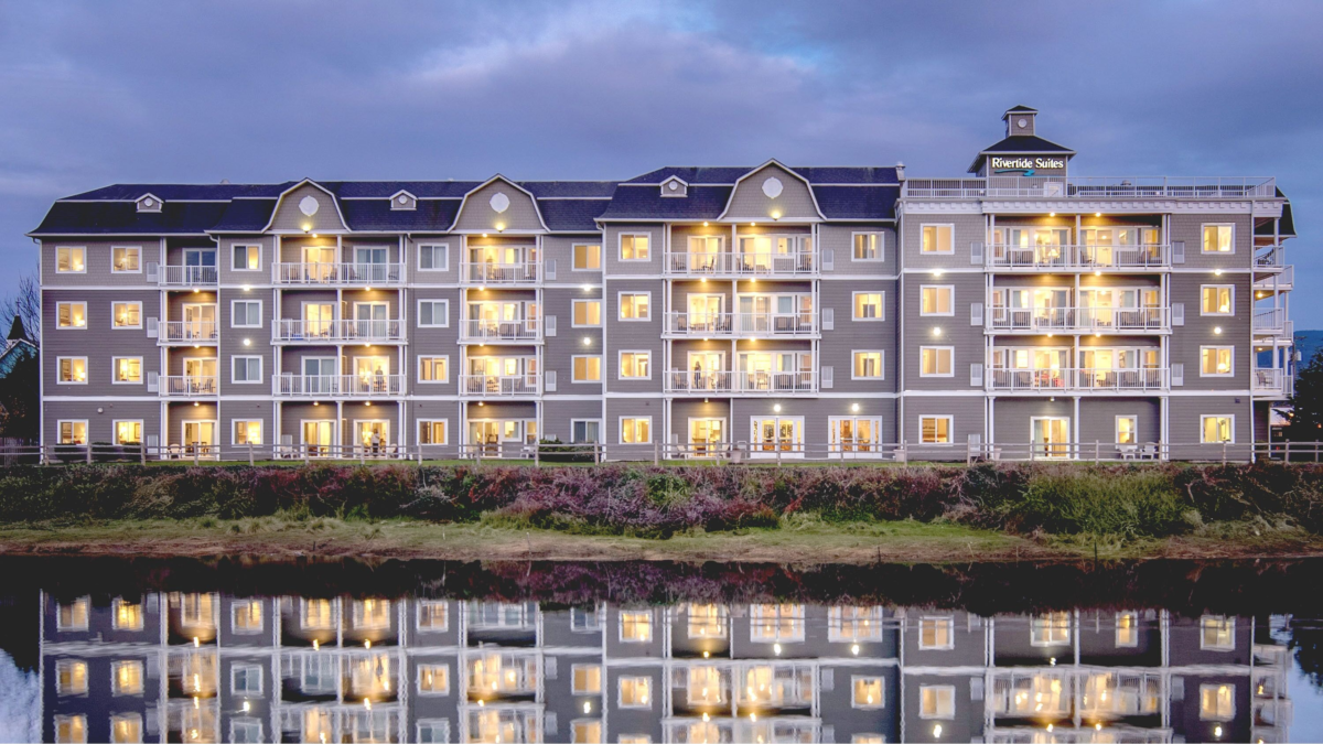 Rivertide Suites Hotel in Seaside Oregon reflected in the river at dusk — modern Oregon Coast lodging with scenic views